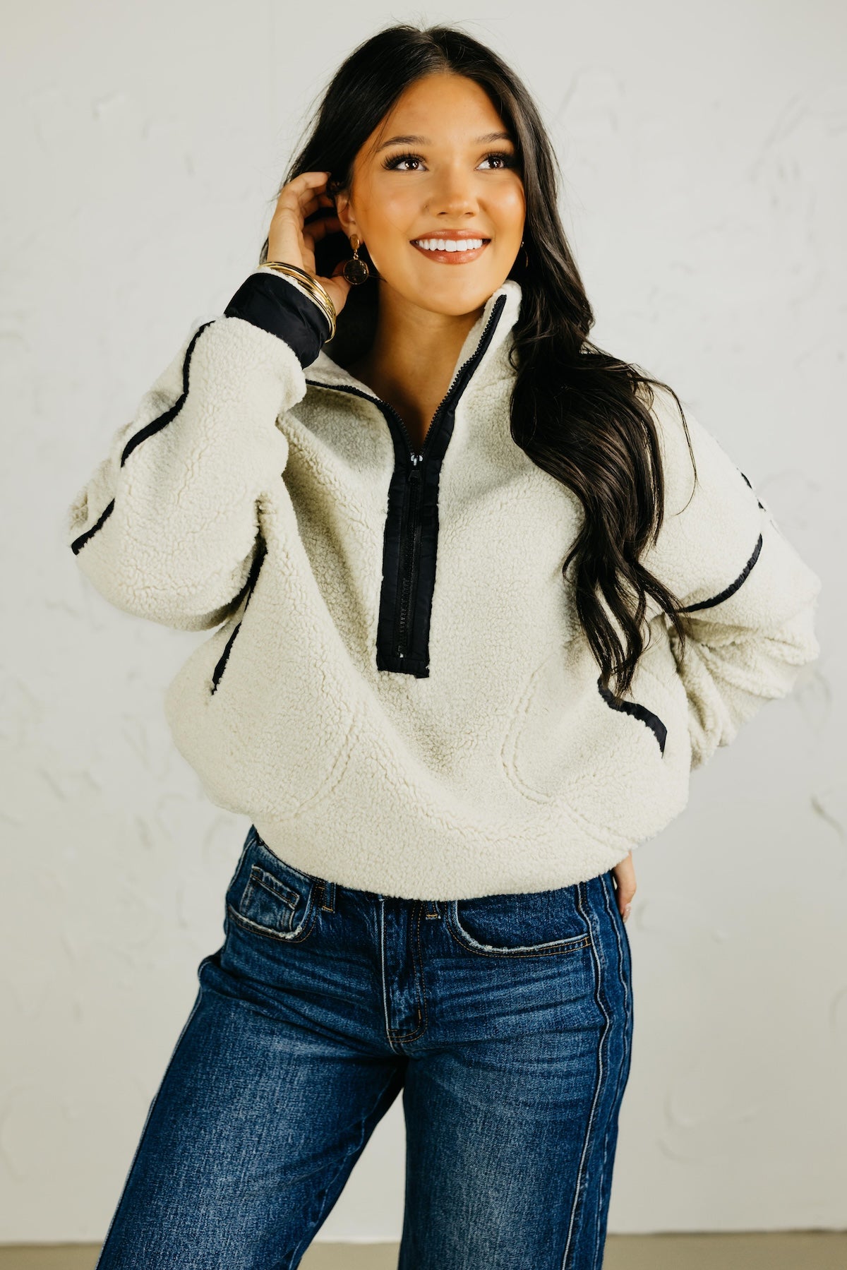 Woman wearing a white fleece pullover with black accents and blue jeans against a plain background