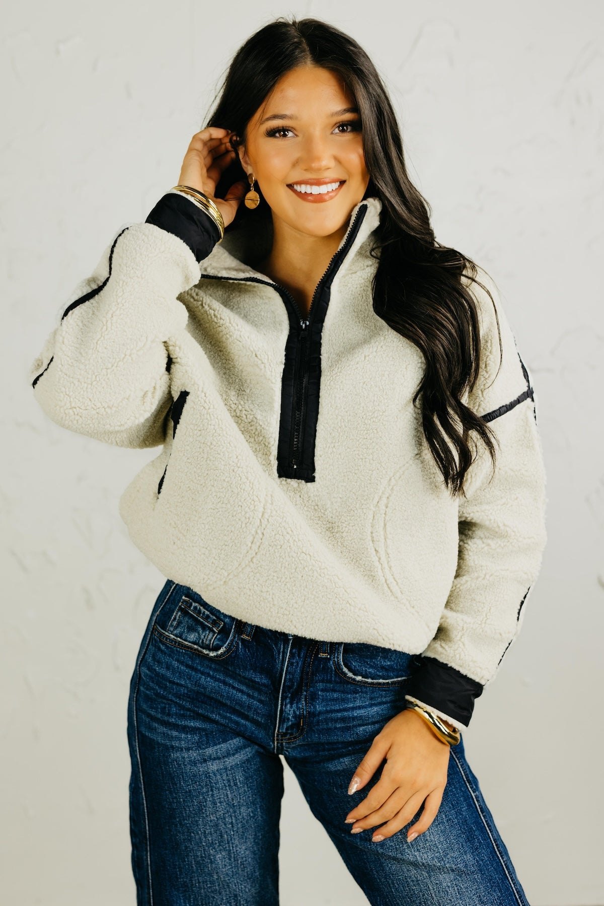 Woman wearing a beige fleece pullover with black accents and blue jeans on a plain background