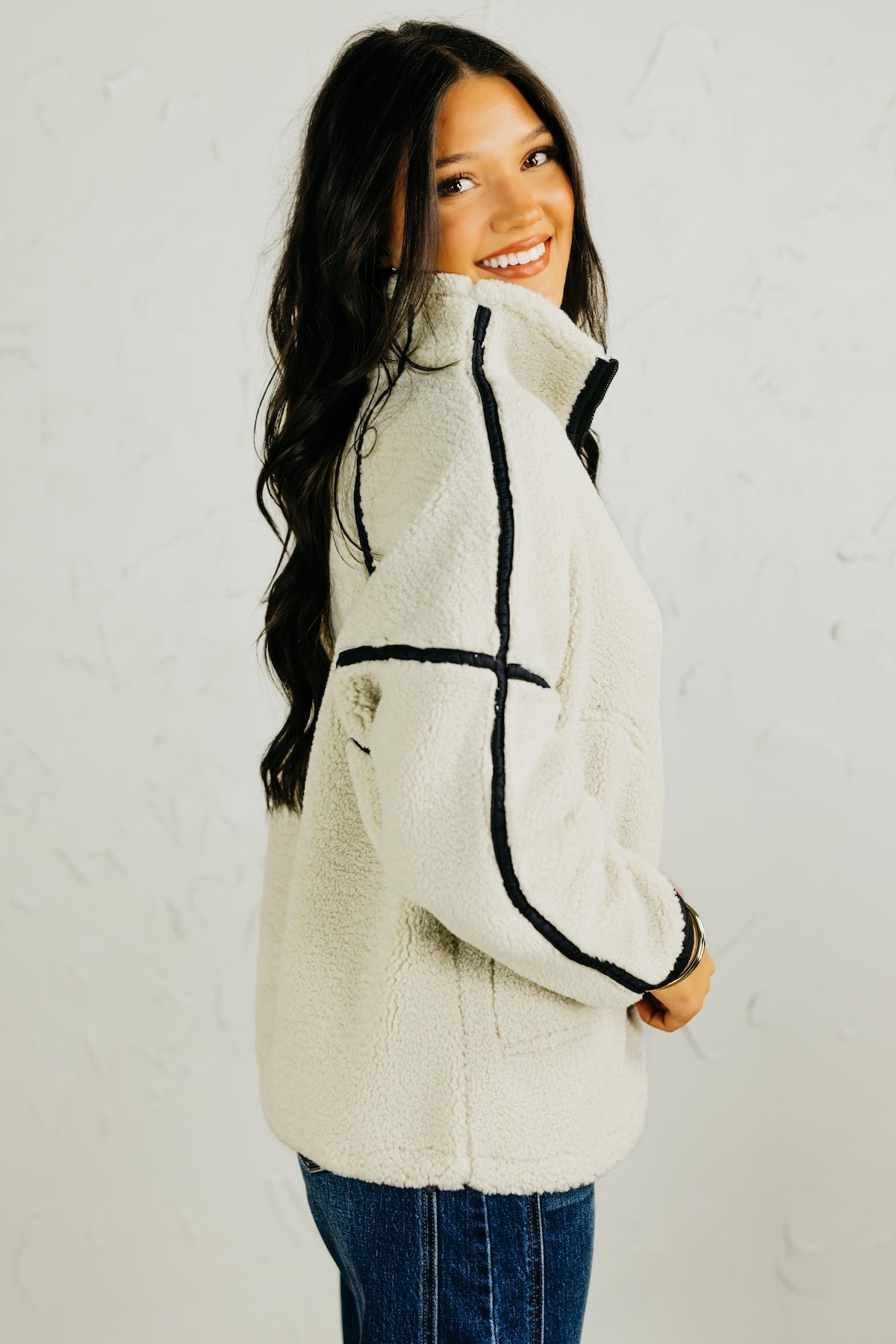 Woman wearing a cream-colored jacket with black accents against a white background