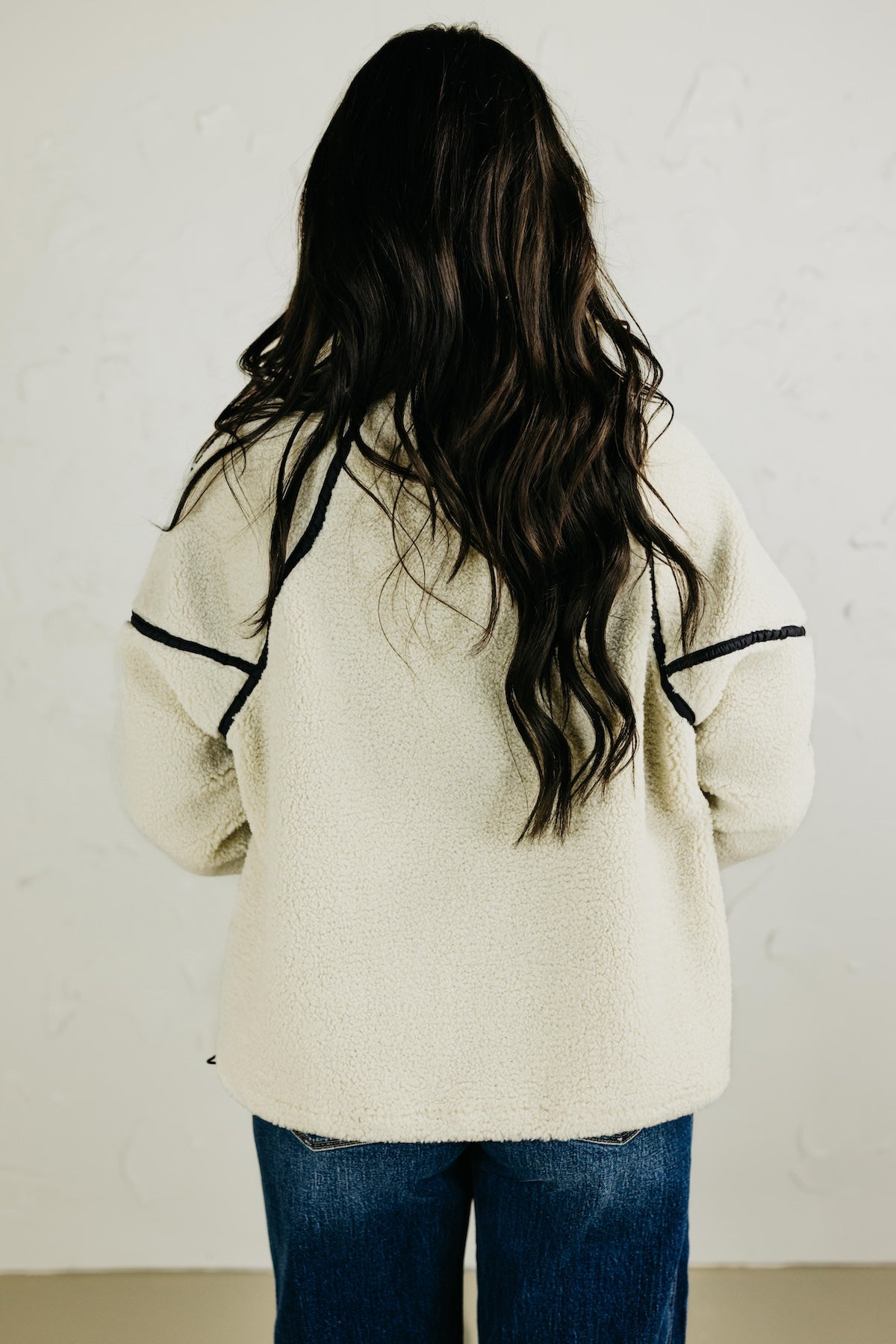 Person wearing a cream-colored sweater with black trim from behind against a plain background