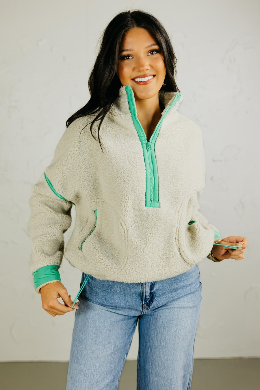 Woman wearing a light gray fleece pullover with green trim against a plain background