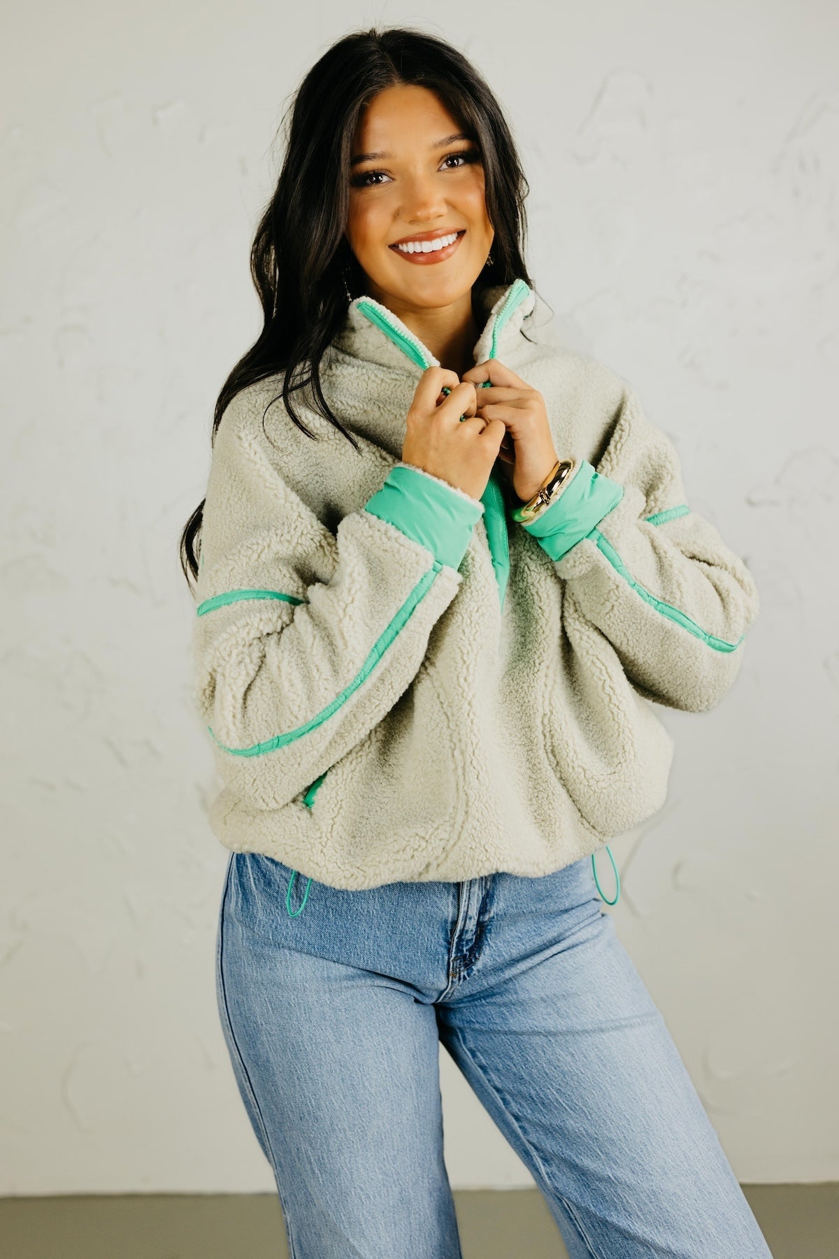 Woman wearing a beige fleece jacket with green trim against a white background