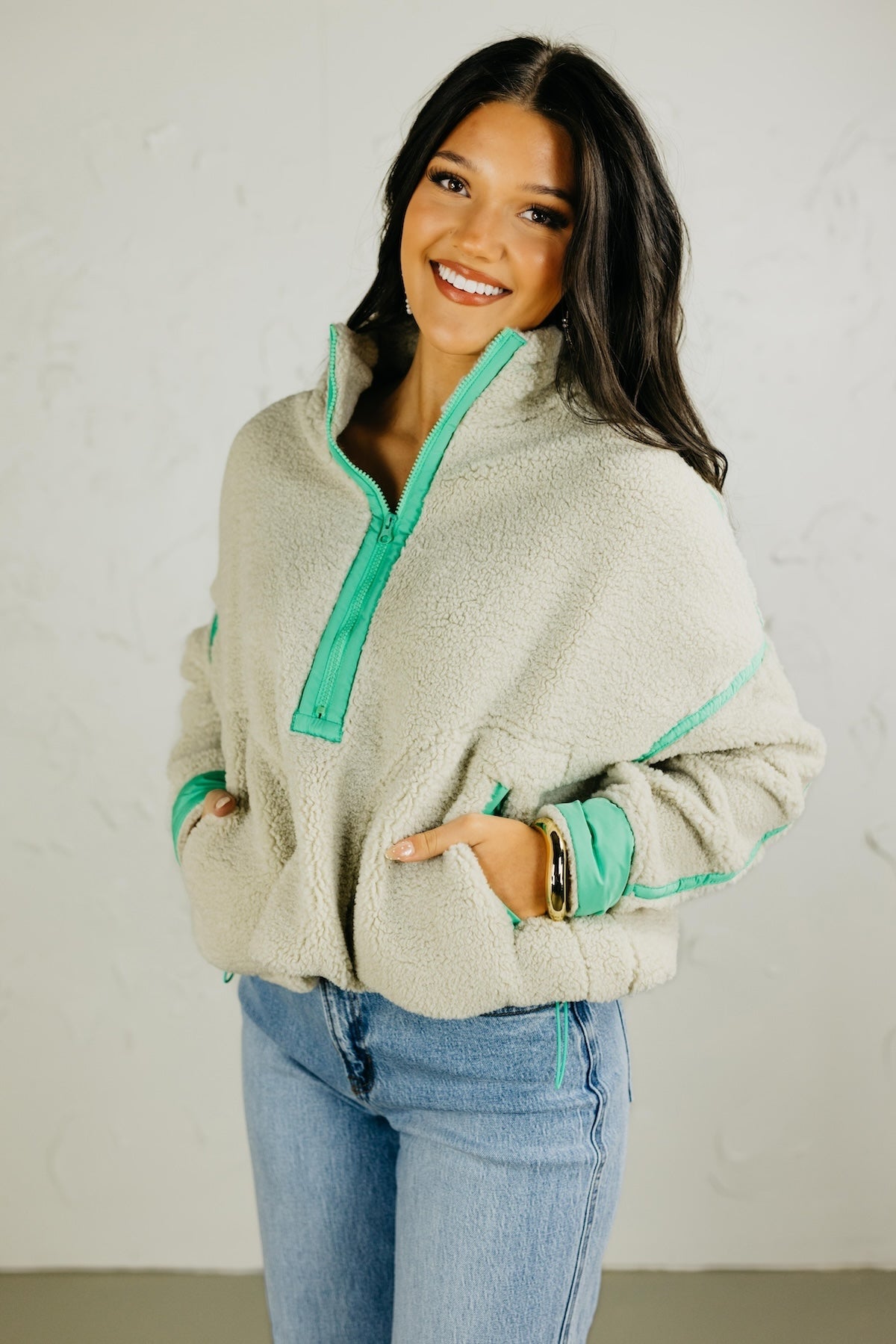 Woman wearing a beige fleece jacket with green trim against a plain background