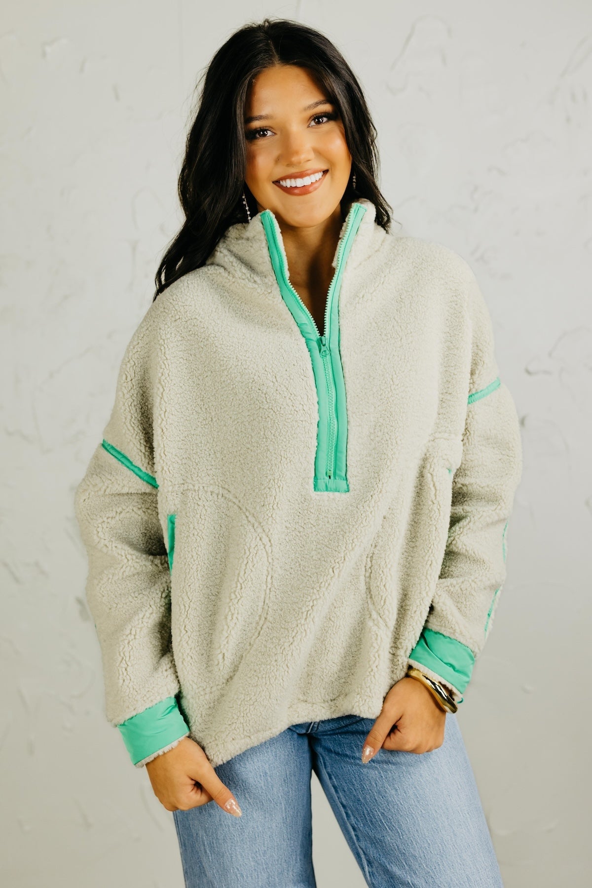 Woman wearing a light gray fleece pullover with green accents against a white background