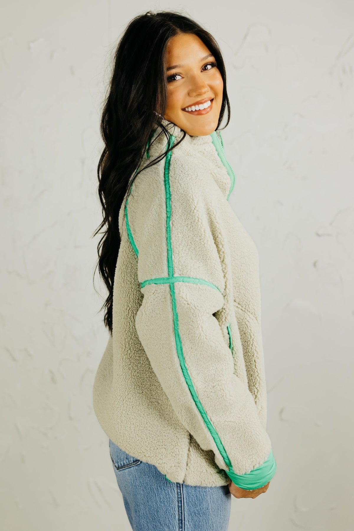 Woman wearing a light-colored fleece jacket with green accents against a plain background