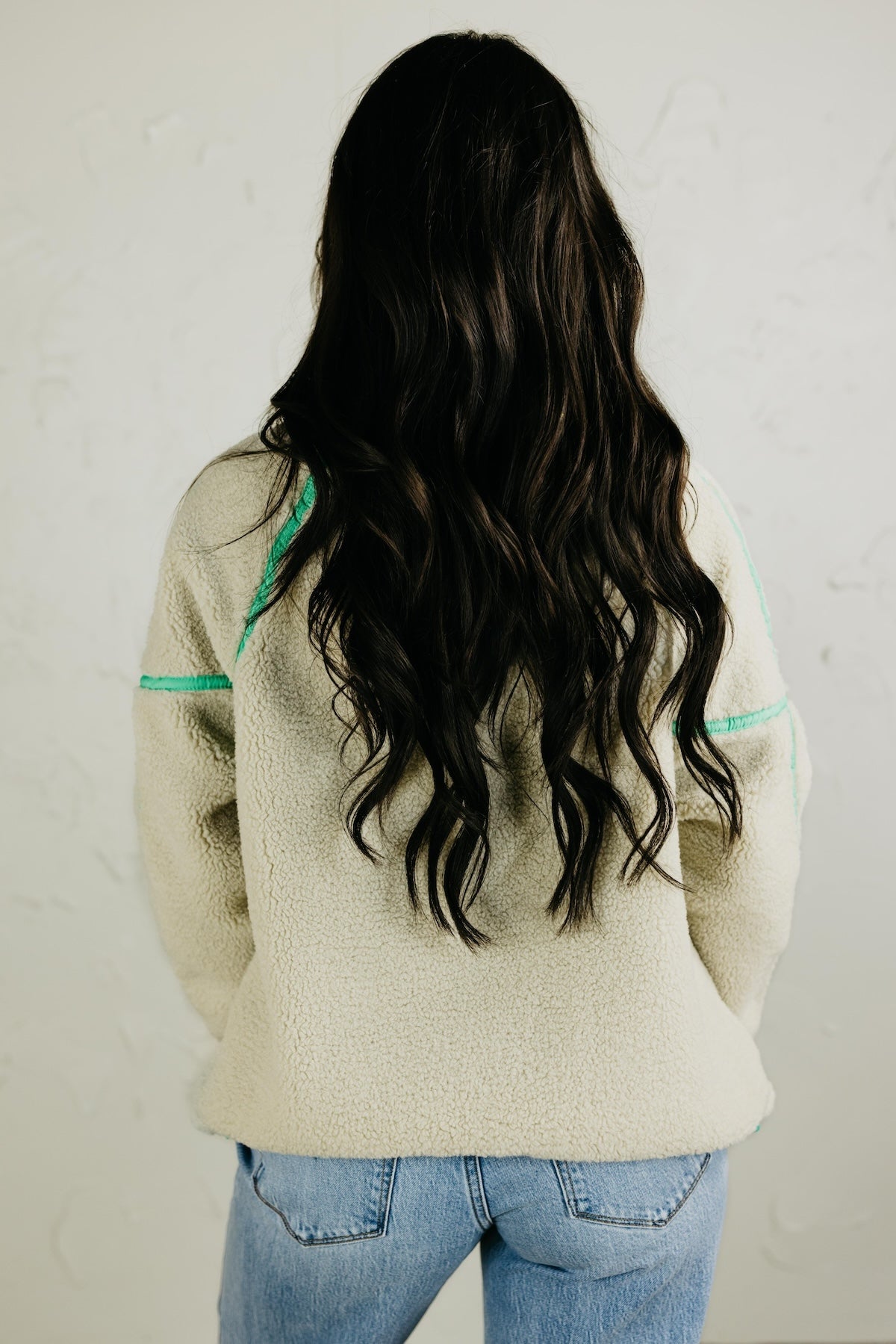 Person wearing a beige fleece jacket with green accents on a plain background