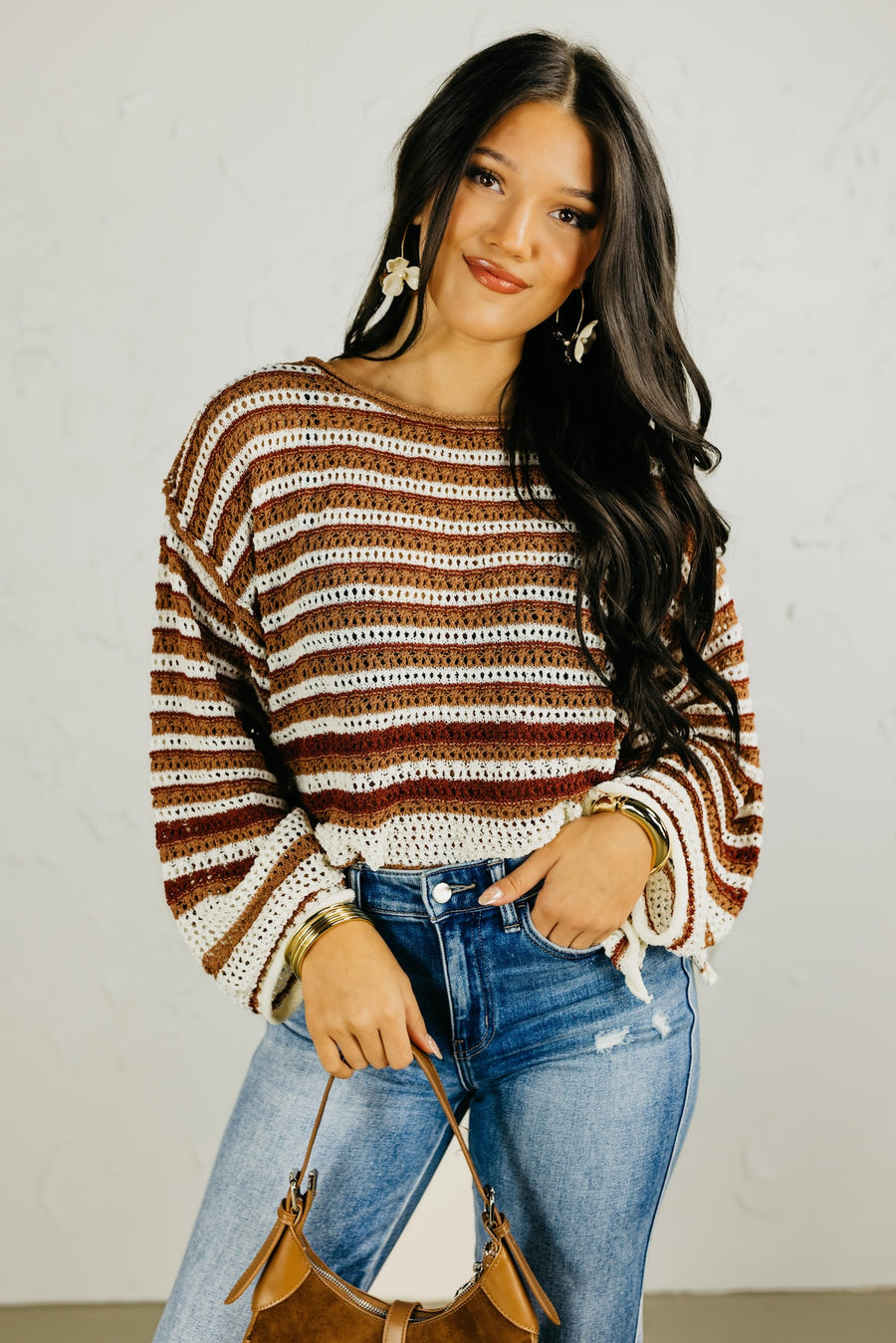 Woman wearing a striped sweater and jeans with a handbag against a plain background