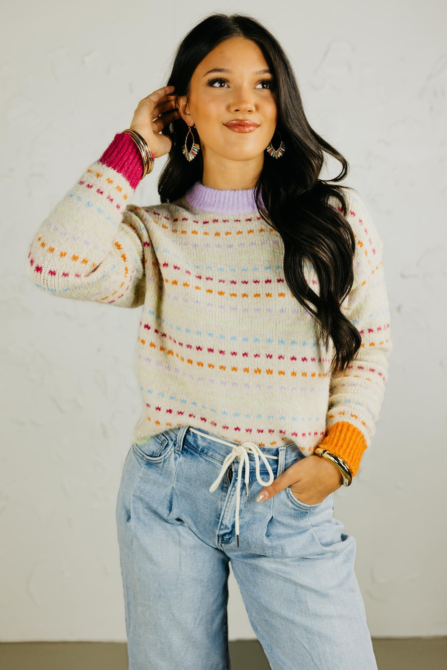 Woman wearing a colorful sweater and light blue jeans against a plain background